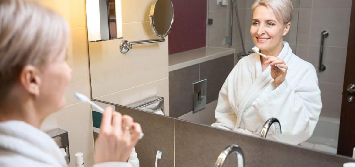 A woman brushing her teeth as part of her daily oral hygiene routine at home between dental visits.