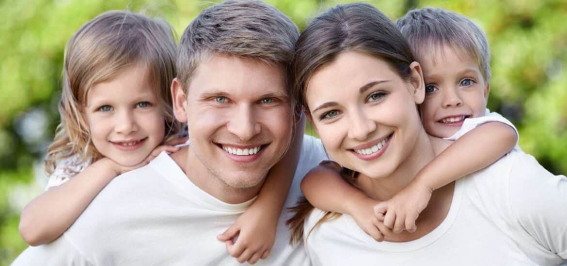 Happy family of four showing healthy smiles that grow with trusted family dentistry.