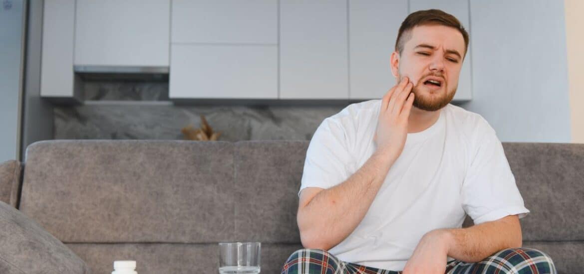 Person holding jaw while managing toothache pain at home.