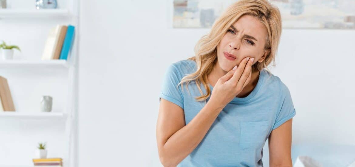 Woman holding her cheek in discomfort due to sudden gum swelling and dental pain at home.