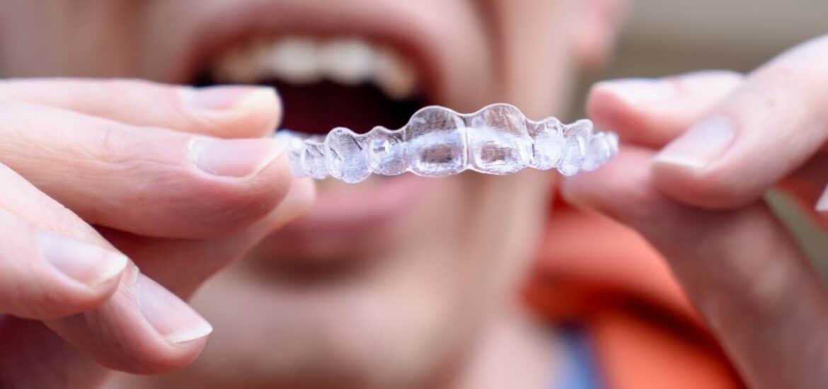 Adult holding clear Invisalign aligners to improve smile confidence and professional appearance.